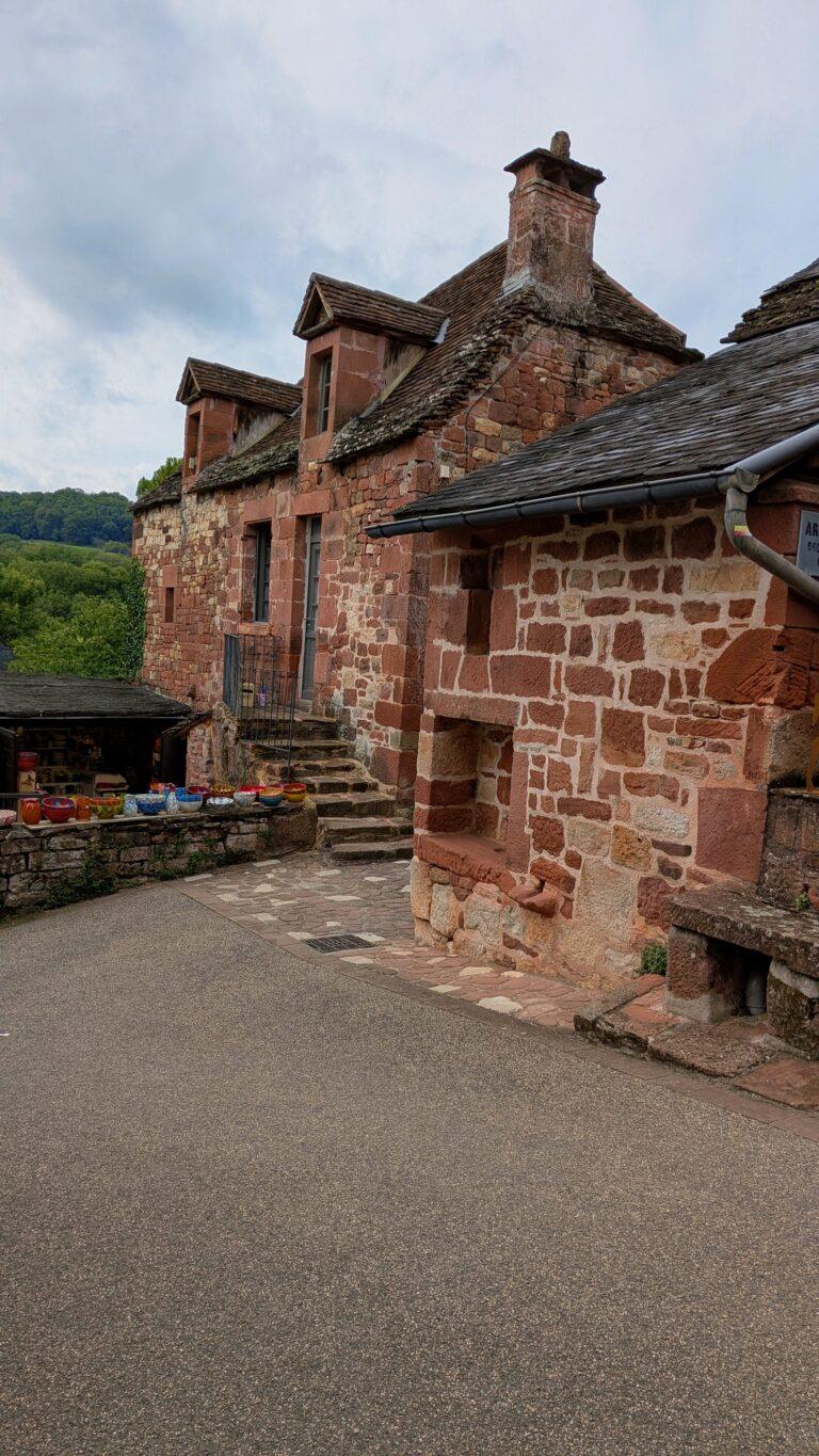 Artisan shop, Collonges-la-Rouge, handmade pottery, local products, Collonges-la-Rouge: The Red Stone Gem of France, Collonges-la-Rouge village, red sandstone houses, medieval architecture, Limousin France, Collonges-la-Rouge alley, red stone walls, flowered balconies, charming street, saru's postcards, beautiful villages of France