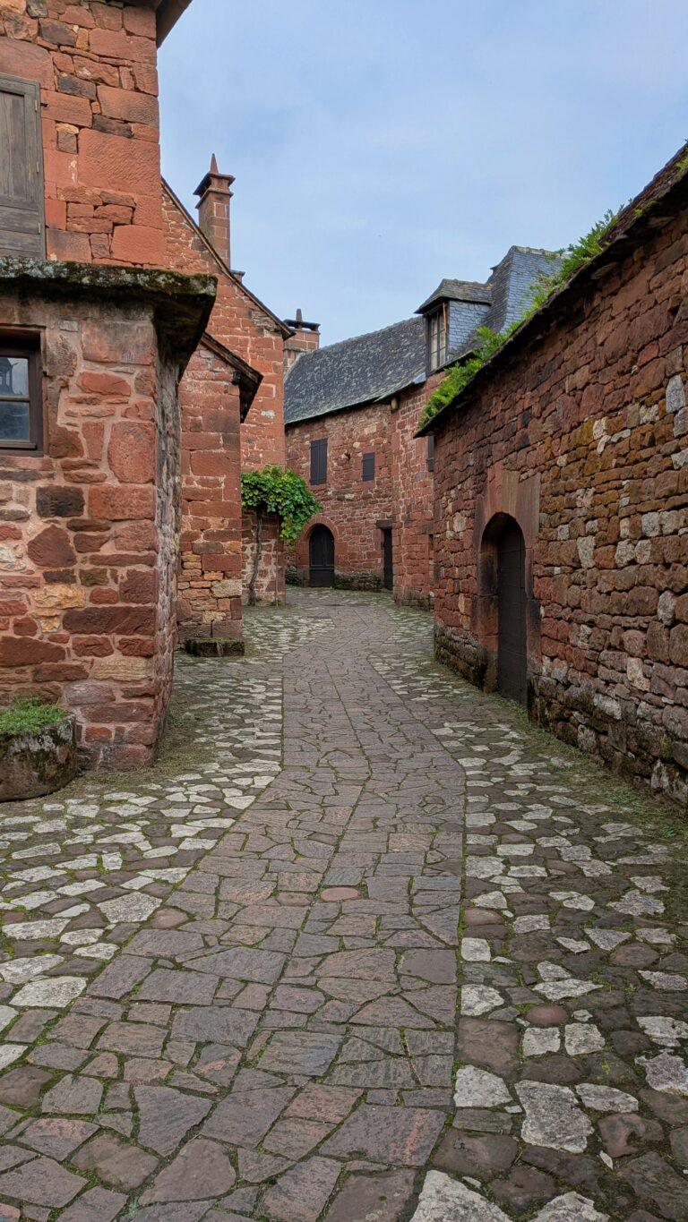 Collonges-la-Rouge alley, red stone walls, flowered balconies, charming street, Collonges-la-Rouge: The Red Stone Gem of France, Collonges-la-Rouge village, red sandstone houses, medieval architecture, Limousin France, Collonges-la-Rouge alley, red stone walls, flowered balconies, charming street, saru's postcards, beautiful villages of France