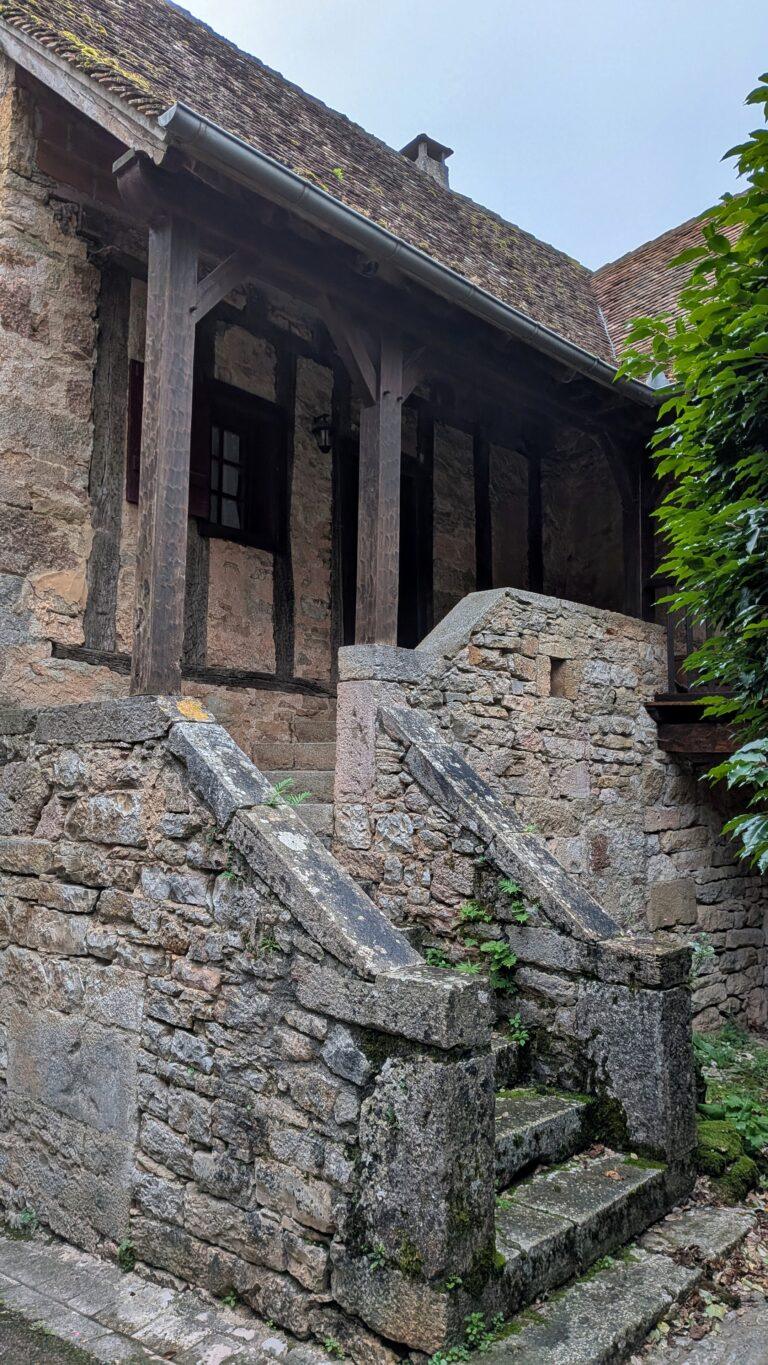 Loubressac: The Hilltop Jewel of the Lot Valley, saru's postcards, church of saint jean baptiste loubressac, romanesque church, historic building, village center, france chateau de loubressac, stone castle, hilltop fortress, panoramic view, French heritage, loubressac viewpoint, valley view, dordogne valley, scenic landscape, lot region lot valley from loubressac, rolling hills, green fields, beautiful france, countryside view, loubressac houses, flowered balconies, limestone walls, charming details, travel destination old wooden door loubressac, rustic french house, village charm, historical architecture, loubressac sunset, golden light, picturesque rooftops, lot countryside, magical moment morning in loubressac, sunlight on stone houses, peaceful atmosphere, hidden gem france village lane loubressac, flowers and ivy, romantic walk, travel photography, postcard moment
